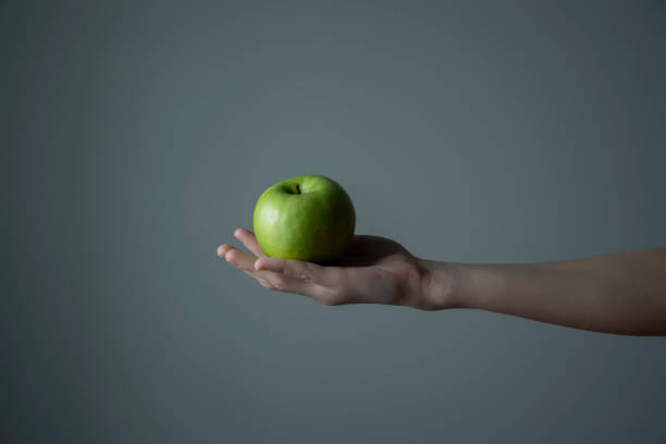 istock Woman`s hand holding green apple grey neutral background - raw photo. 1306192103
