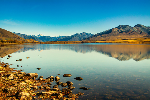 The snow capped mountain peaks of Southern Alps reflected in calm still water on Lake Clearwater, Ashburton Lakes high country