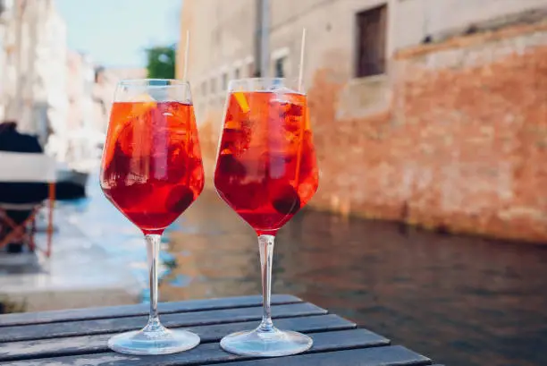 Photo of Two glasses of Spritz Veneziano cocktail served near the Venetian canal.  Popular italian summer aperitif drink.