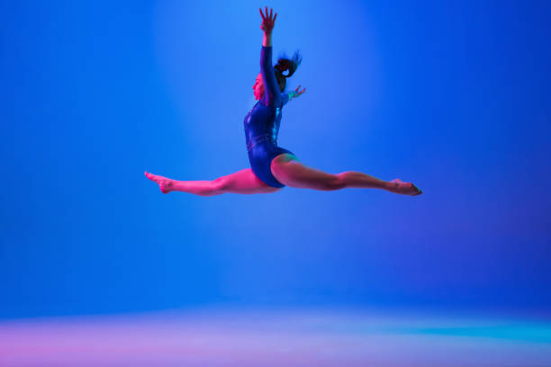 istock Young flexible girl isolated on blue studio background. Young female model practicing artistic gymnastics. Exercises for flexibility, balance. 1306193719