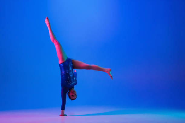 istock Young flexible girl isolated on blue studio background. Young female model practicing artistic gymnastics. Exercises for flexibility, balance. 1306193738