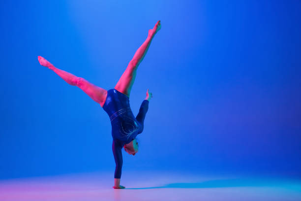 istock Young flexible girl isolated on blue studio background. Young female model practicing artistic gymnastics. Exercises for flexibility, balance. 1306193744
