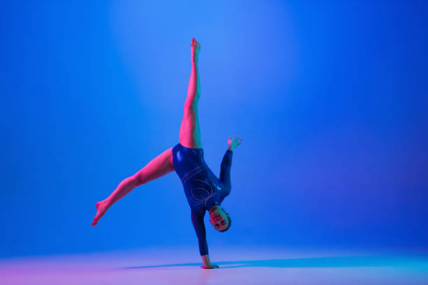 istock Young flexible girl isolated on blue studio background. Young female model practicing artistic gymnastics. Exercises for flexibility, balance. 1306193763