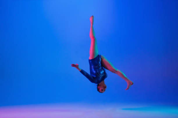 istock Young flexible girl isolated on blue studio background. Young female model practicing artistic gymnastics. Exercises for flexibility, balance. 1306193764