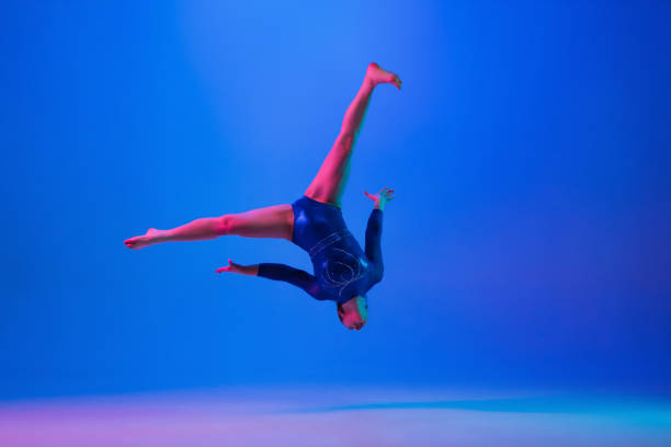 istock Young flexible girl isolated on blue studio background. Young female model practicing artistic gymnastics. Exercises for flexibility, balance. 1306193772