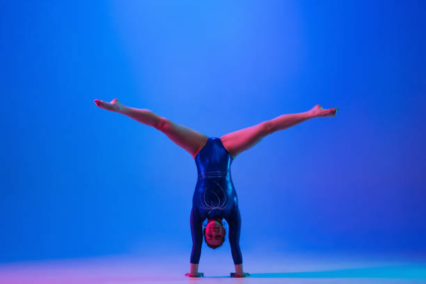 istock Young flexible girl isolated on blue studio background. Young female model practicing artistic gymnastics. Exercises for flexibility, balance. 1306193777