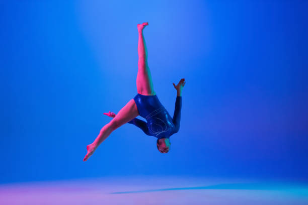 istock Young flexible girl isolated on blue studio background. Young female model practicing artistic gymnastics. Exercises for flexibility, balance. 1306194217