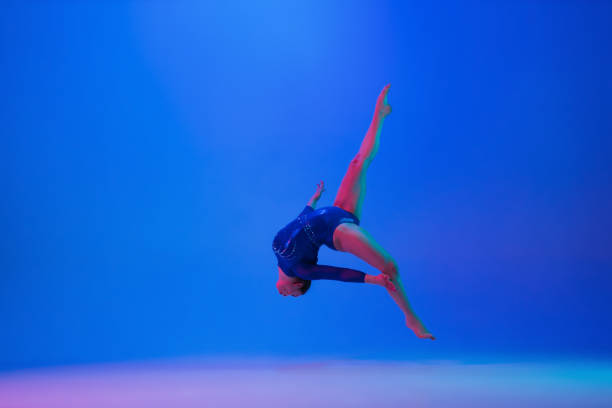 istock Young flexible girl isolated on blue studio background. Young female model practicing artistic gymnastics. Exercises for flexibility, balance. 1306194298
