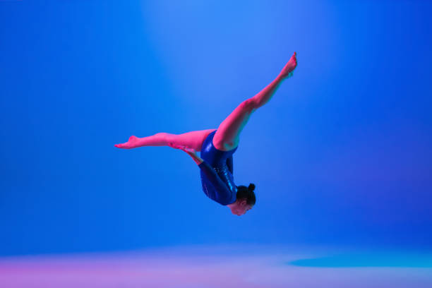 istock Young flexible girl isolated on blue studio background. Young female model practicing artistic gymnastics. Exercises for flexibility, balance. 1306194319