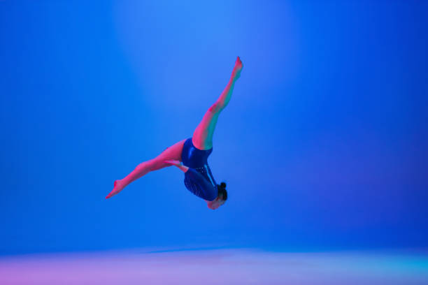 istock Young flexible girl isolated on blue studio background. Young female model practicing artistic gymnastics. Exercises for flexibility, balance. 1306194342