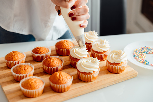 istock Woman decorates freshly baked cupcakes with cream 1306194391