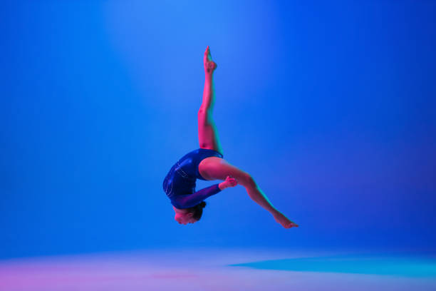 istock Young flexible girl isolated on blue studio background. Young female model practicing artistic gymnastics. Exercises for flexibility, balance. 1306194448