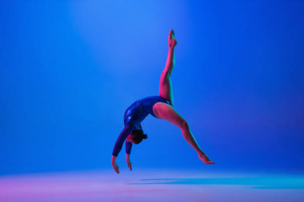 istock Young flexible girl isolated on blue studio background. Young female model practicing artistic gymnastics. Exercises for flexibility, balance. 1306194495