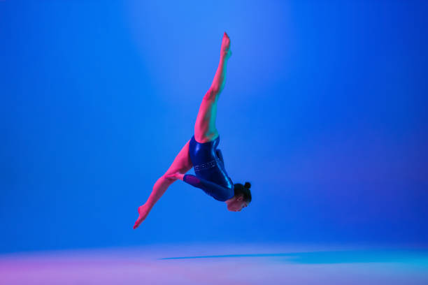 istock Young flexible girl isolated on blue studio background. Young female model practicing artistic gymnastics. Exercises for flexibility, balance. 1306194502