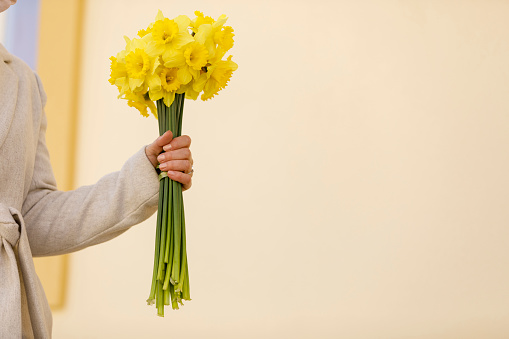 Cut out shot of unrecognizable woman taking a walk on the city street and carrying a beautiful bouquet of yellow daffodils.
