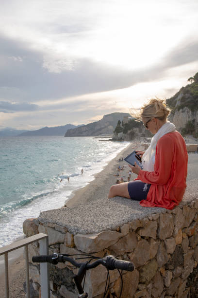 istock Woman sits on balcony above beach and uses digital tablet 1306197323