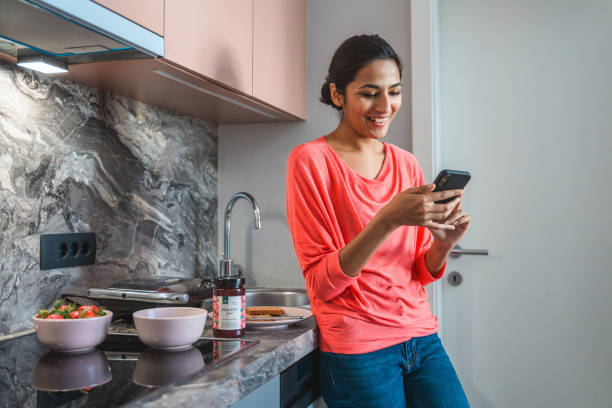 istock Young Indian Woman Preparing Breakfast and Using Mobile Phone in Domestic Kitchen 1306198284