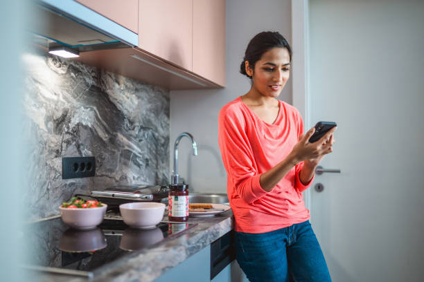 istock Young Indian Woman Preparing Breakfast and Using Mobile Phone in Domestic Kitchen 1306198287