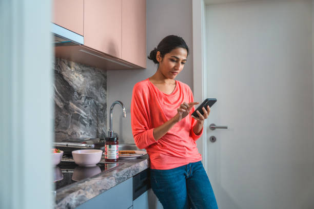 istock Young Indian Woman Preparing Breakfast and Using Mobile Phone in Domestic Kitchen 1306198290