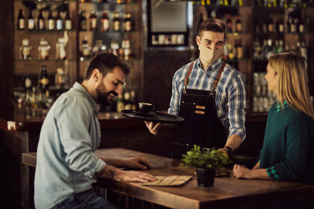 istock Happy waiter wearing protective face mask while serving coffee to customers in a cafe. 1306198823