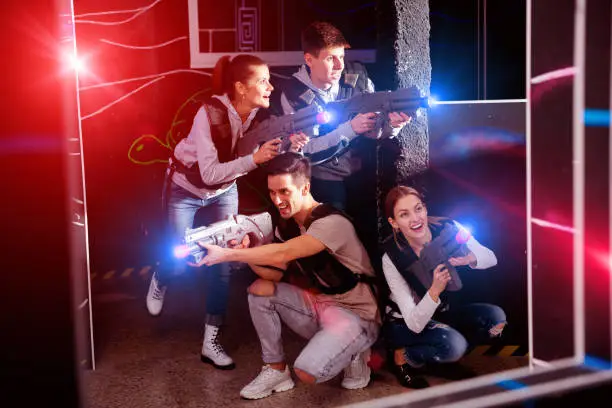 Photo of Happy young people with laser pistols posing together on dark la