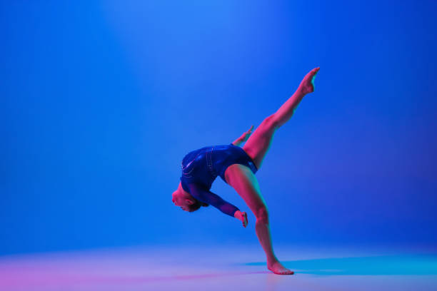 istock Young flexible girl isolated on blue studio background. Young female model practicing artistic gymnastics. Exercises for flexibility, balance. 1306203634
