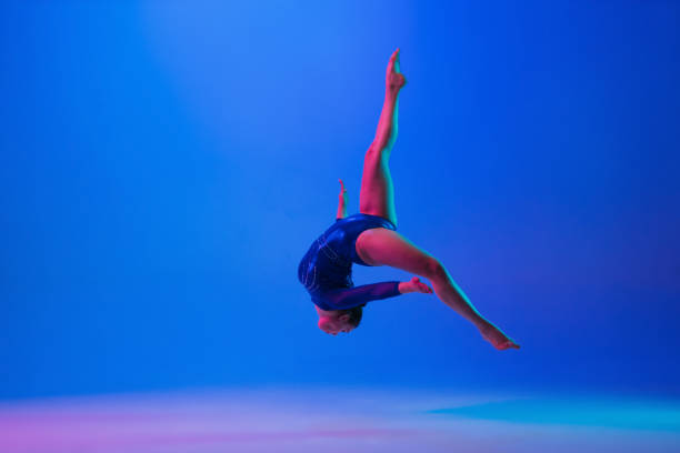 istock Young flexible girl isolated on blue studio background. Young female model practicing artistic gymnastics. Exercises for flexibility, balance. 1306203637