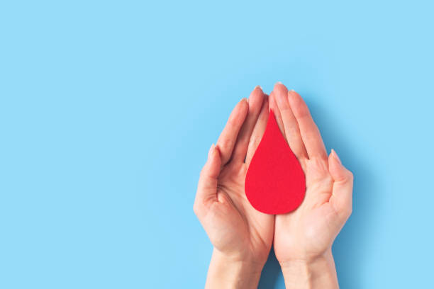kırmızı kan damla simbol ve mavi arka plan üzerinde eller ile dünya hemofili günü konsepti - kan bağışı stok fotoğraflar ve resimler