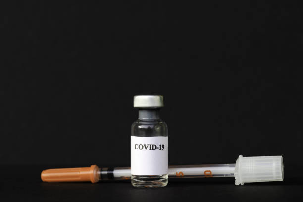 a corona vaccine ampoule and syringe against a black background - injecting flu virus cold and flu doctors office imagens e fotografias de stock