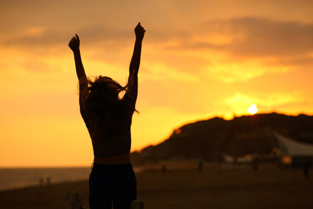 silhouette de femme soulevant des bras célébrant au coucher du soleil - arms outstretched arms raised women winning photos et images de collection