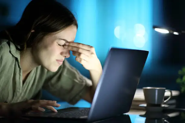 Fatigued woman suffering eyestrain using laptop at night