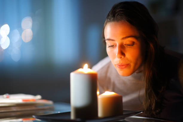 mujer soplando velas en casa en la noche - vela equipo de iluminación fotografías e imágenes de stock