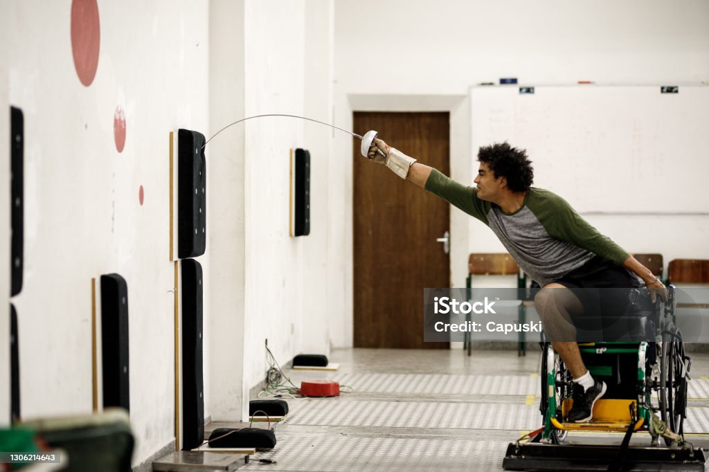 One legged male wheelchair fencing athlete training lunge on wall equipment Wheelchair fencing athletes training Athlete with Disabilities Stock Photo