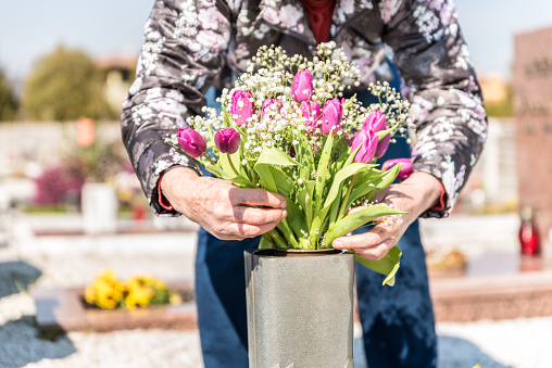 Senior Woman During COVID-19 Pandemic Bringing Fresh Flower on the Family Grave at the Cemetery