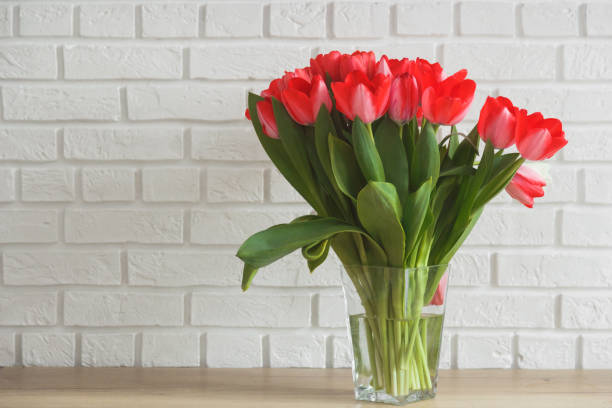 istock Pink tulips in glass vase on background white brick wall. 1306215850