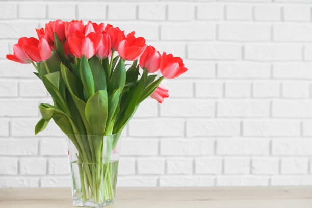 istock Pink tulips in glass vase on background white brick wall. 1306215870