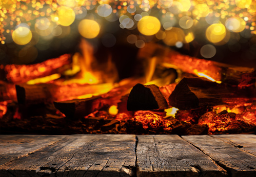 Empty rustic wooden table with defocused lights and fire in the fireplace on background. Holiday backdrop for product display on top of the table. Focus on foreground.