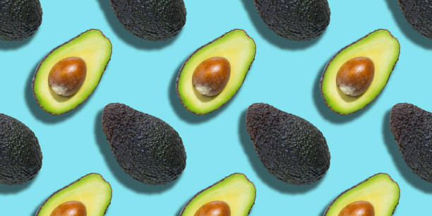 istock Seamless pattern of fresh ripe green avocado isolated on blue background. Top view. Banner. Flat lay composition. Pop art design. Creative summer food background 1306217738