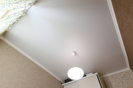 Stretch white matte ceiling close-up with a chandelier in the interior of a rectangular room