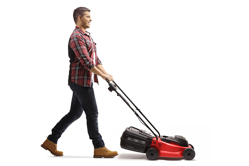 Full length profile shot of a young man working with a lawnmower isolated on white background