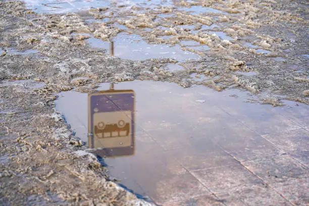 Photo of Muddy sidewalk and reflection of bus stop sign in puddle