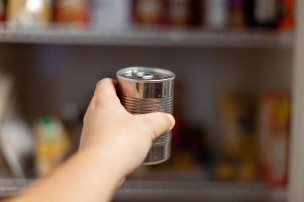 A human hand holds a can of food for storage in the kitchen pantry.