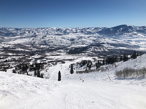 Looking down a slope at Snowbasin ski resort in northern Utah, with a snow-covered mountain range in the distance.