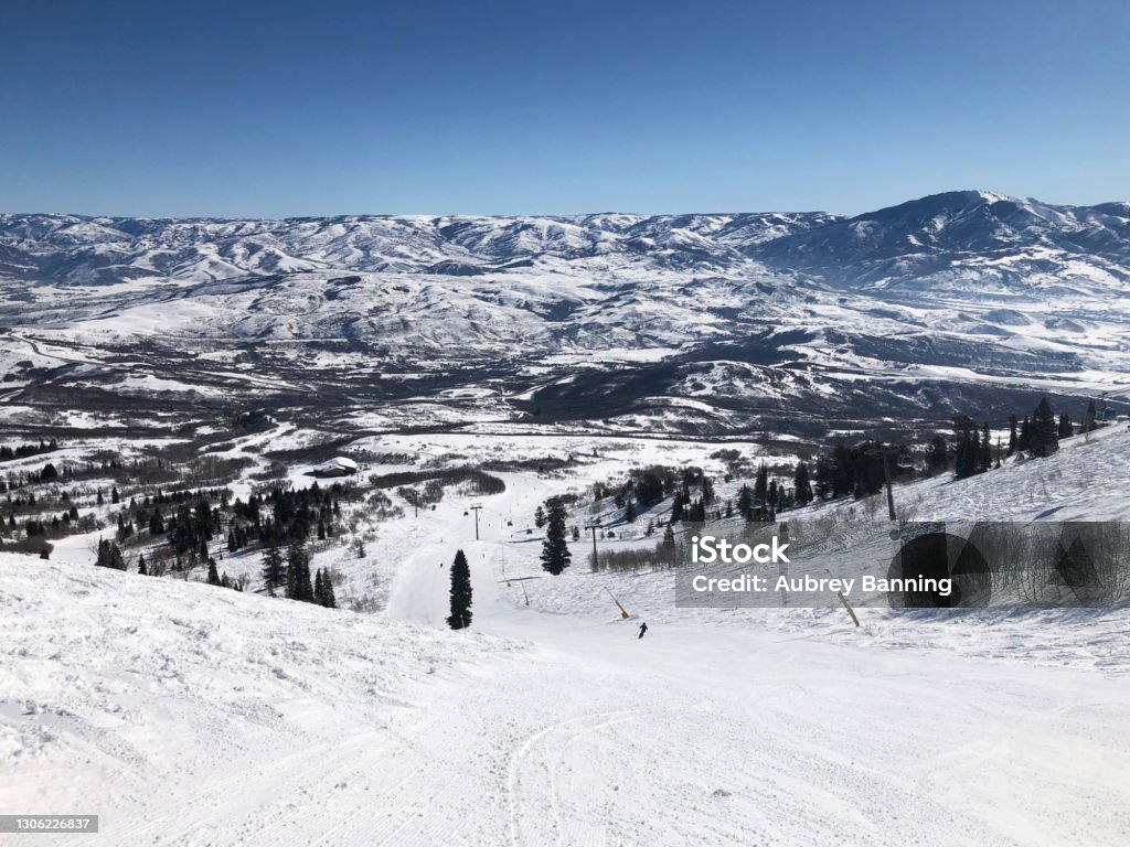 Ski Slope Overlooking Snow-capped Mountains Looking down a slope at Snowbasin ski resort in northern Utah, with a snow-covered mountain range in the distance. Ogden - Utah Stock Photo