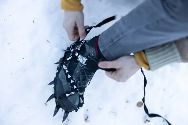 Winter hiking equipment for ice walk. Hiker putting Crampons on Hiking Boots outdoors.