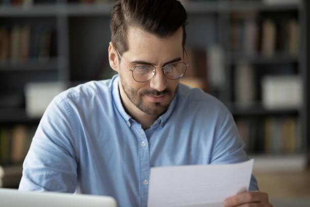 Serious man sitting at workplace reading formal business letter