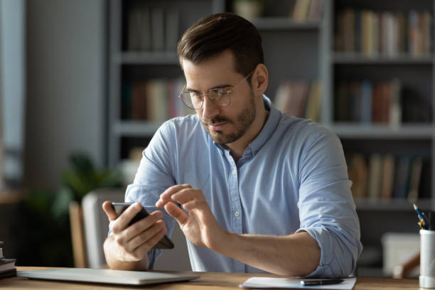 istock Serious businessman wearing spectacles using mobile phone sit at desk 1306230743