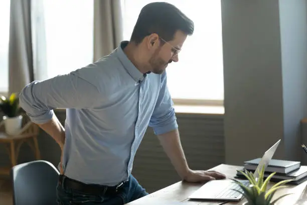 Businessman touches lower back feeling pain sudden ache while get up out of office chair, muscular spasm, strain caused by sedentary lifestyle, prolonged inactivity, sit in incorrect posture concept