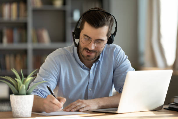 istock Man wear headphones watch webinar using laptop writing notes 1306230767