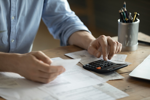Personal finance management, accounting concept. Close up view man sitting at table using calculator performs arithmetic operations calculates costs per month, manage family budget, control expenses